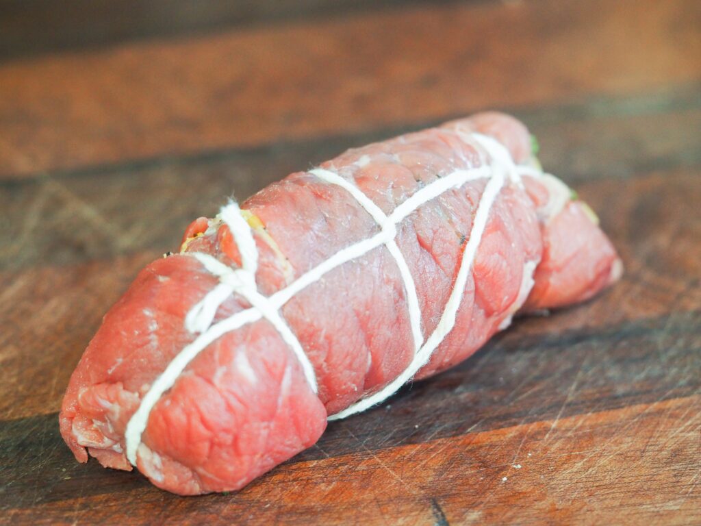 beef roll tied with kitchen twine on wooden cutting board