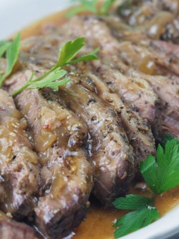 close side view of sliced beef brisket on white platter with gravy sprinked with flat leaf parsley