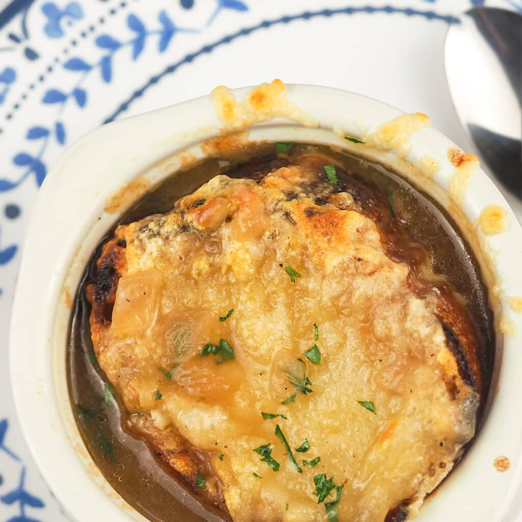 onion soup with cheesy crouton on top sitting on plate with blue flower rim