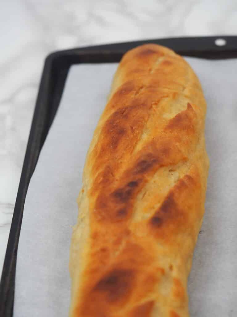single loaf of french bread on baking sheet covered in parchment paper on marlbe counter