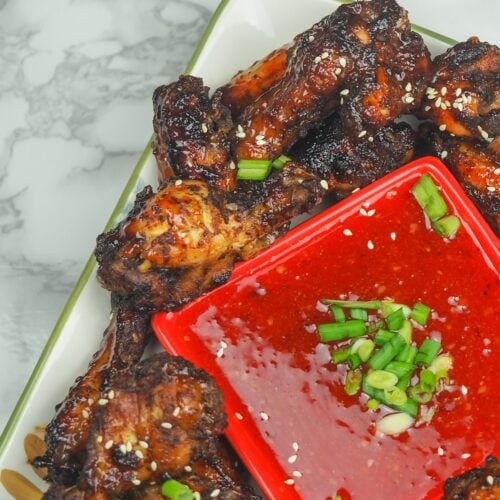 overhead view of cooked chicken wings on platter set to the right at an angle with sweet chili dipping sauce in the middle