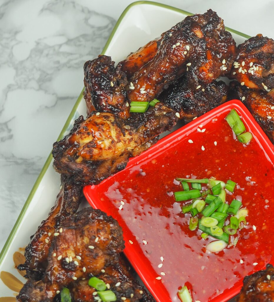 overhead view of cooked chicken wings on platter set to the right at an angle with sweet chili dipping sauce in the middle