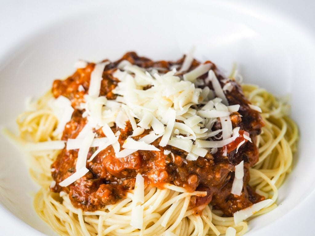close view of spaghetti topped with red meat sauce and fresh grated parmesan cheese