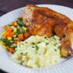 roasted leg quarter on white plate with mashed potatoes and mixed vegetables