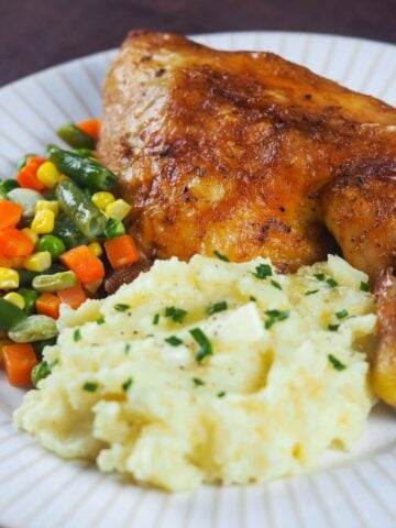 roasted leg quarter on white plate with mashed potatoes and mixed vegetables