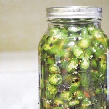 jar of pickled peppers offset to the right on wooden cutting board