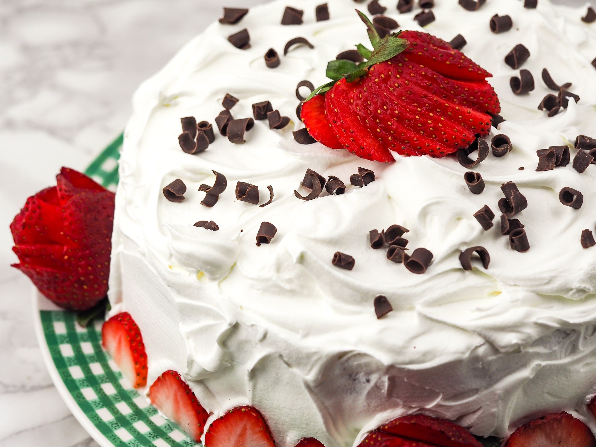 picture of cake offset to right with whipped topping, chocolate curls, and sliced strawberries shaped like roses as accents