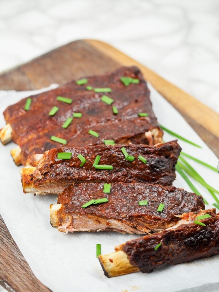 long vertical image of a rack of ribs on top of parchment paper on cutting board