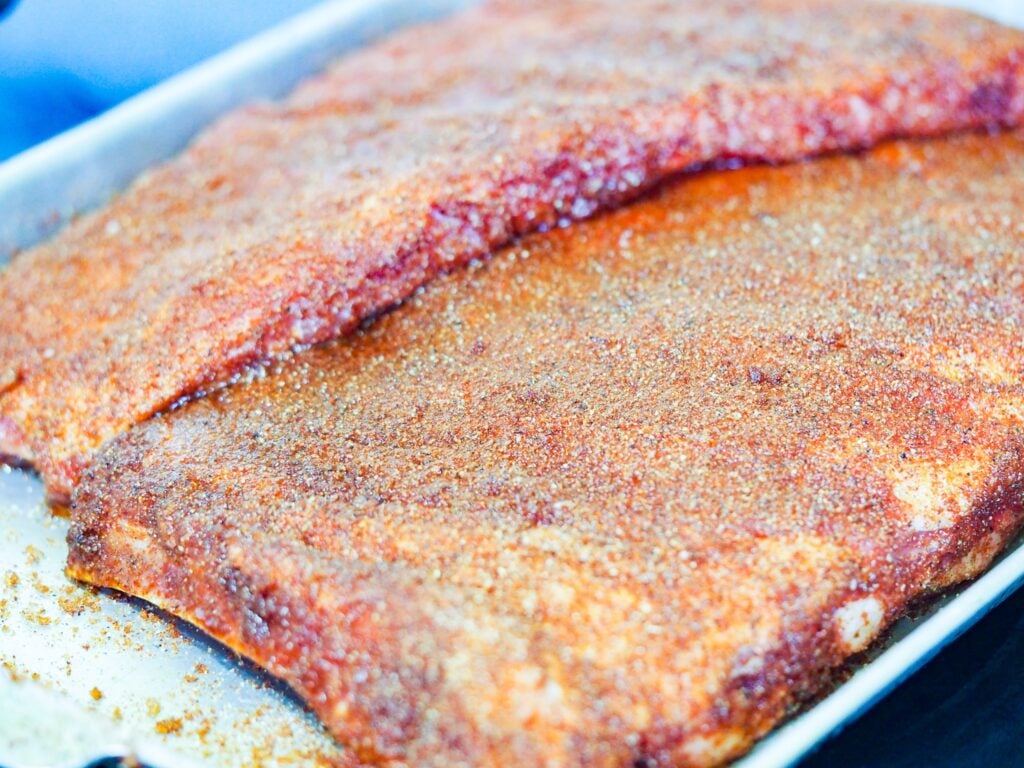 Two racks of seasoned ribs on baking sheet
