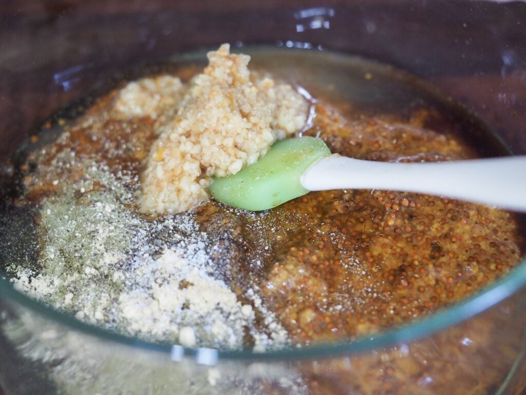 mustard rub ingredients in clear medium mixing bowl with green and white spatula