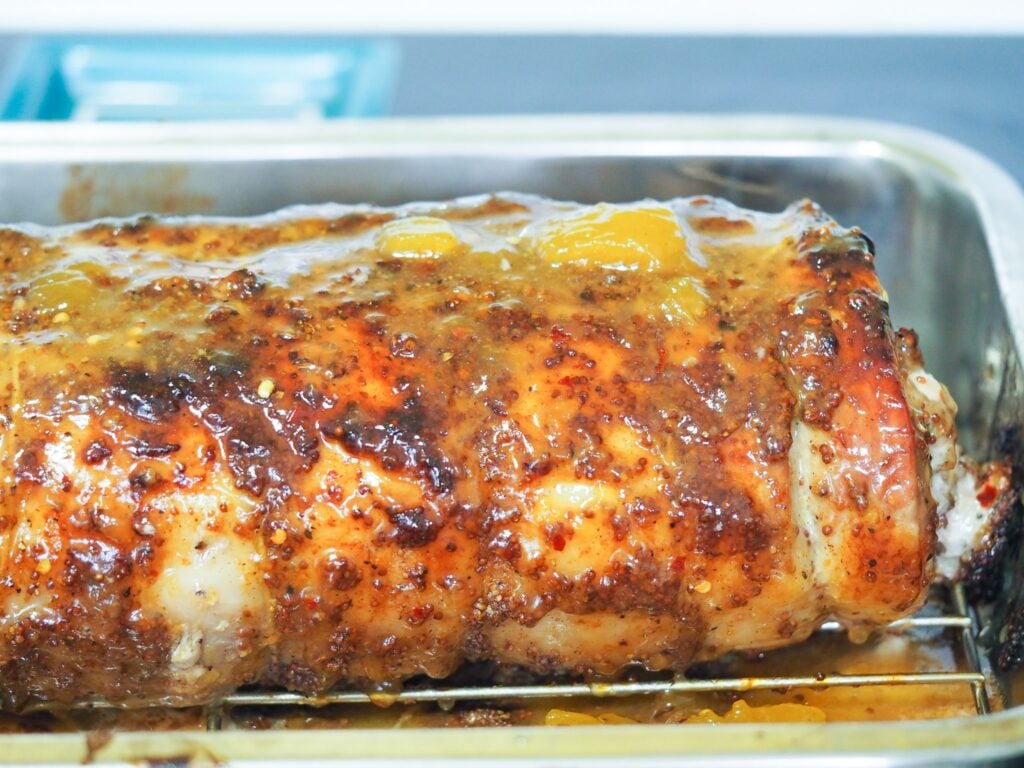 side view of finished pork roast in stainless steel roasting pan on stove top