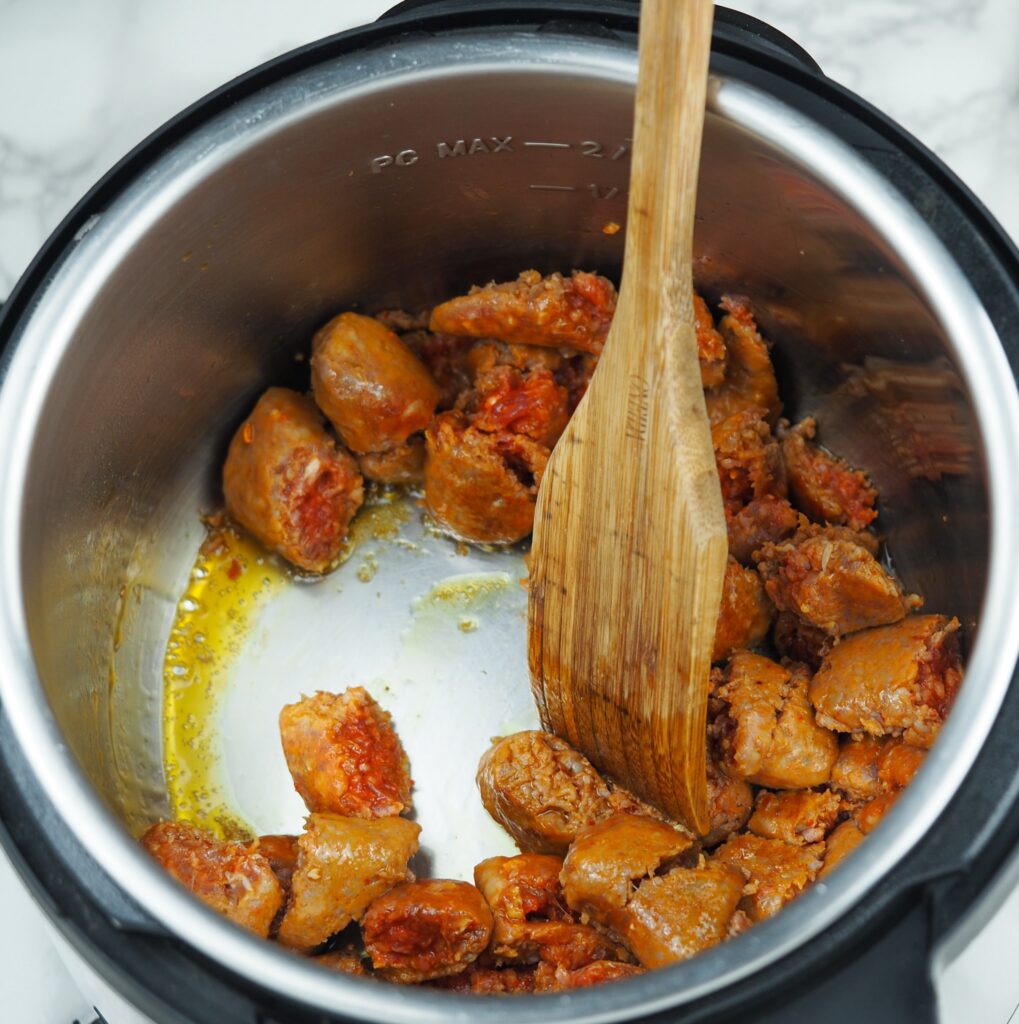 overhead view of cooking chunked Italian sausage in the Instant Pot on saute with wooden spatula