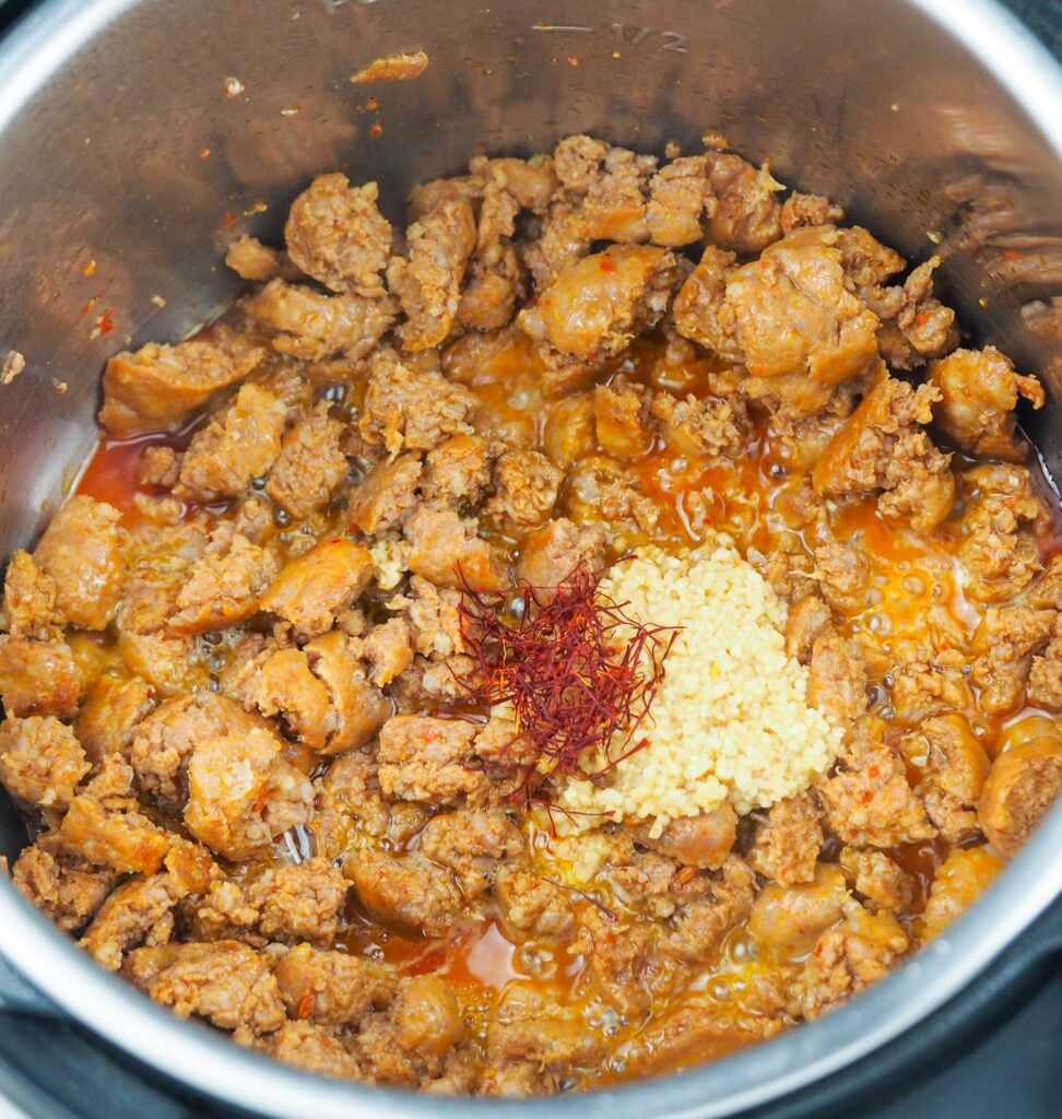 overhead view of cooked Italian sausage in Instant Pot with minced garlic, saffron, and spices