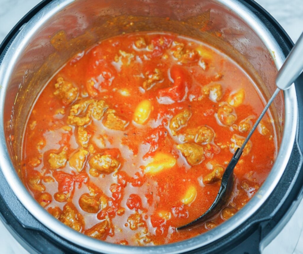 overhead view of sausage gnocchi stew in pressure cooker with spoon