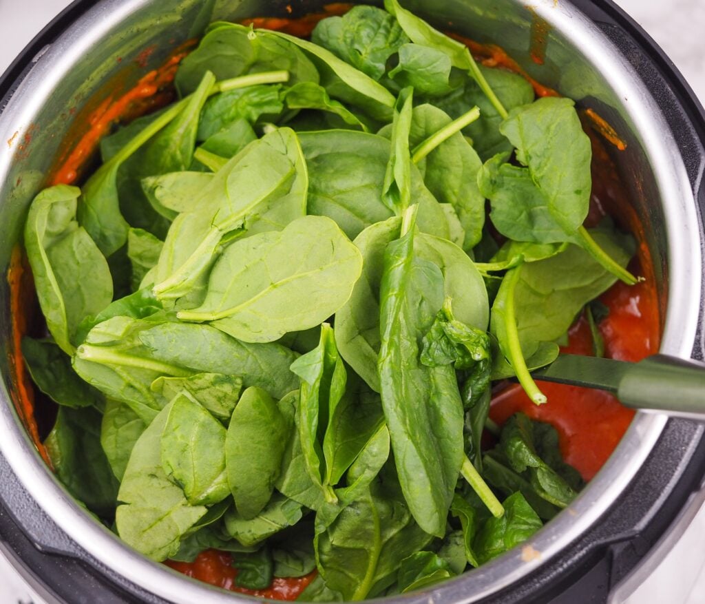 overhead view of stew in Instant Pot topped with raw baby spinach