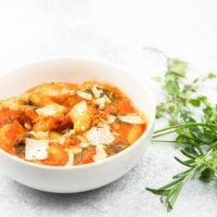 bowl of soup offset to the left with fresh herbs to the righ