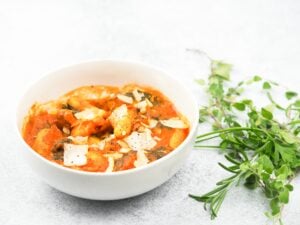 bowl of soup offset to the left with fresh herbs to the righ