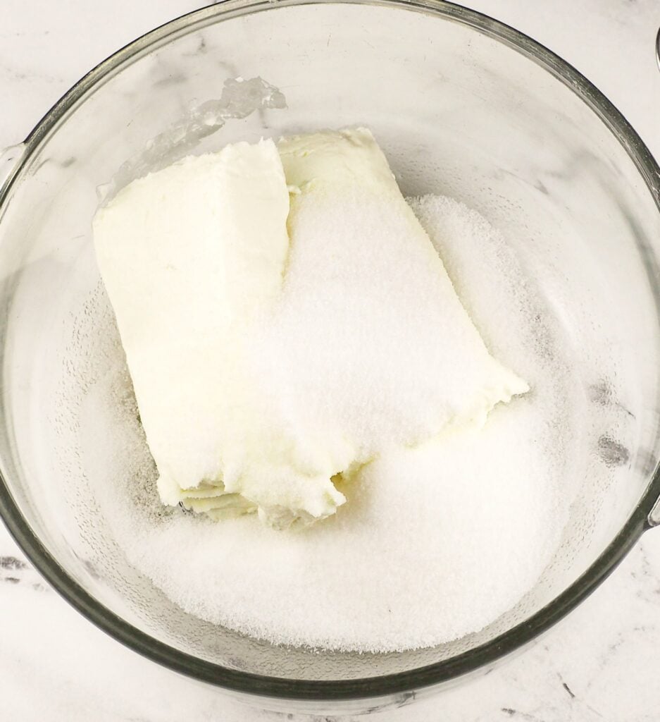 overhead view of cream cheese and sugar in large mixing bowl on marble countertop