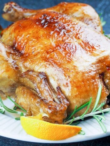 roasted whole chicken on white platter surround by orange quarters and fresh rosemary on black background