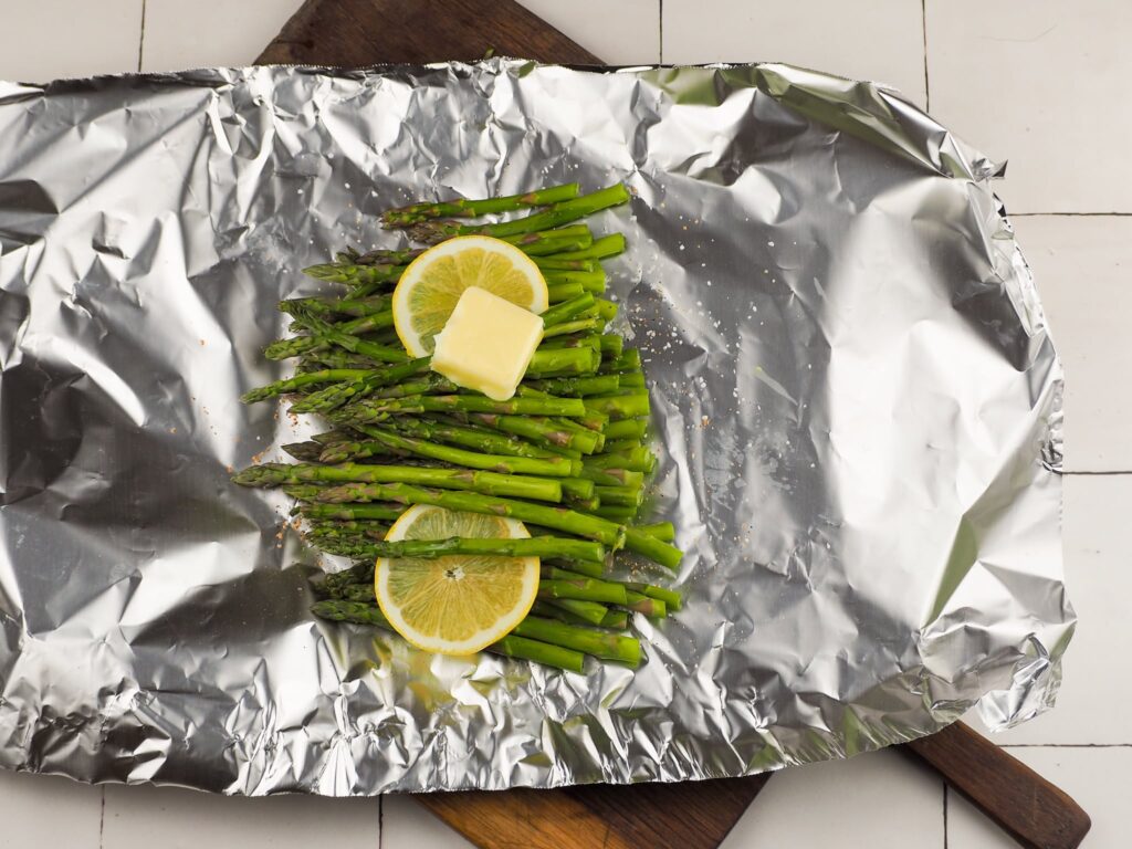 asparagus with lemon and butter on top of foil on cutting board