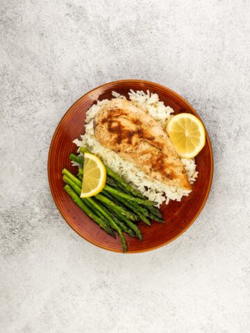 lemon chicken on bed of rice with asparagus on brown dinner plate