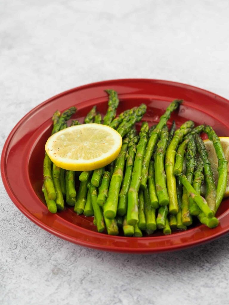 cooked asparagus on red dinner plate with two slices of lemon