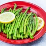cooked asparagus on red dinner plate with two slices of lemon on each side