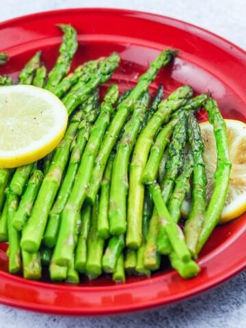 cooked asparagus on red dinner plate with two slices of lemon on each side