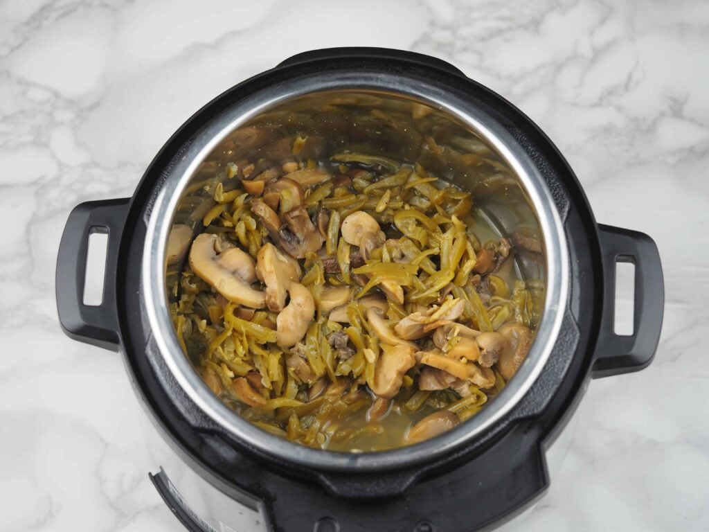 overhead view of green beans, mushrooms, and chicken broth in instant pot
