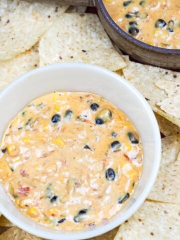 two bowls of queso dip on red platter with tortilla chips