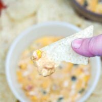 chip suspended above bowl with queso on it