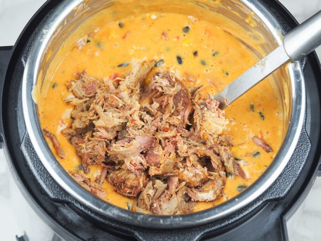 overhead view of smoked pulled pork being added to queso dip