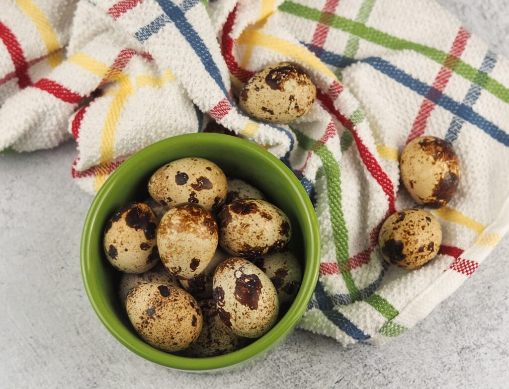 quail eggs in green cup on grey counter with multi colored towel