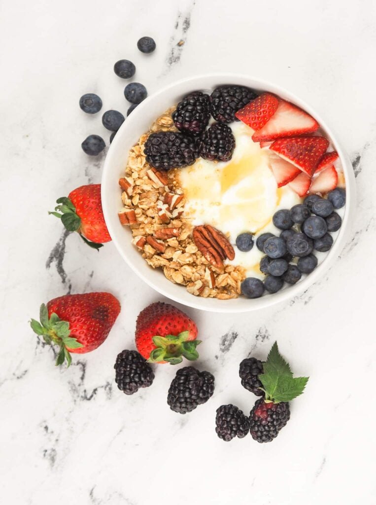 overhead view of finished yogurt bowl on marble countertop surrounded by fresh berries