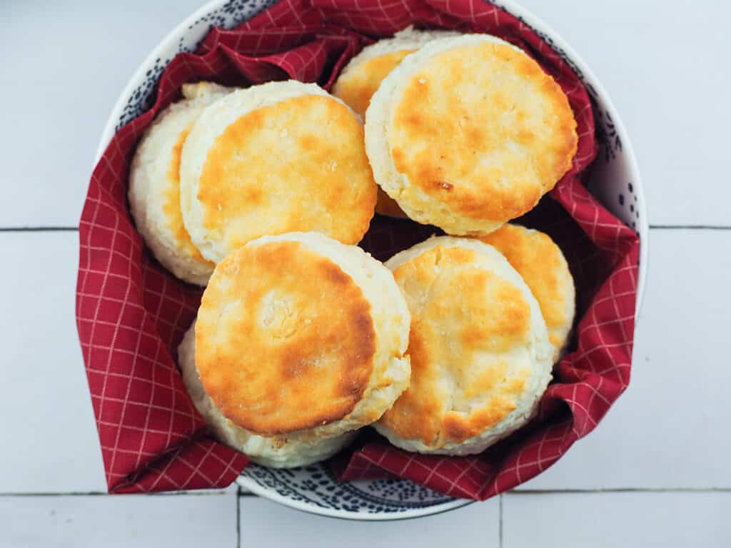 buttermilk biscuits in white bowl with dark blue paisley designs resting on a red cloth with white gridlines