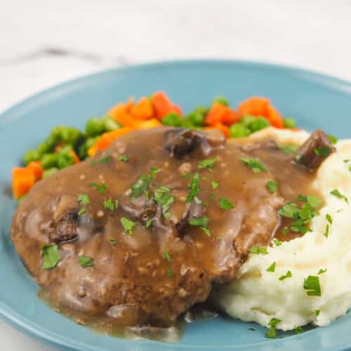 smothered cubed steak on blue plate with mashed potatoes and vegetables
