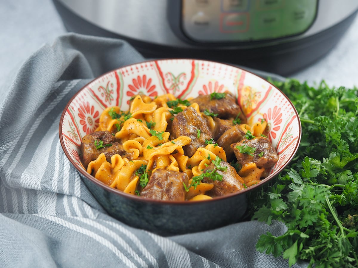 bowl of beef stroganoff sitting in front of Instant Pot with parsley and towel