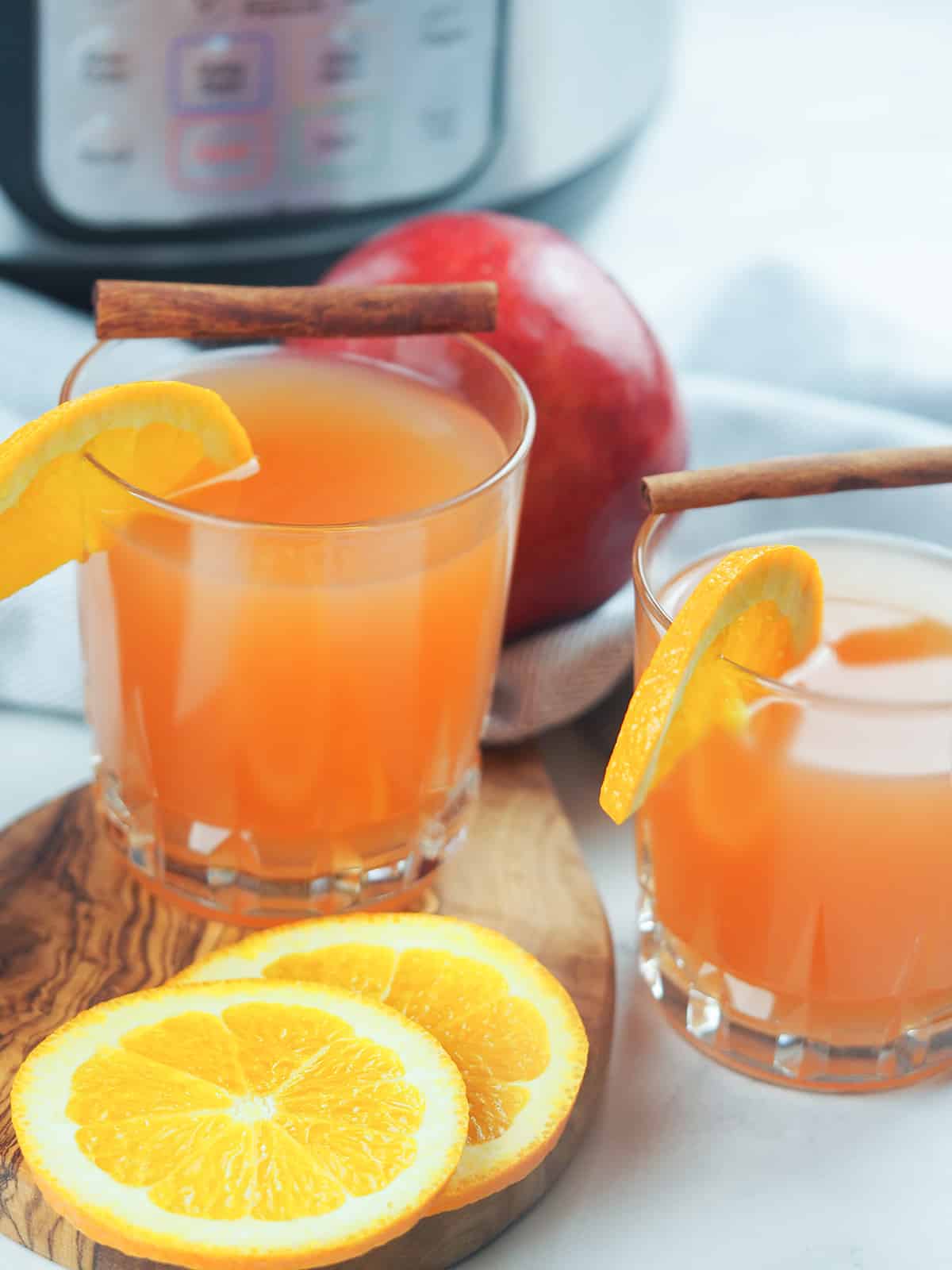 two glasses of apple cider in front of instant pot with orange slices