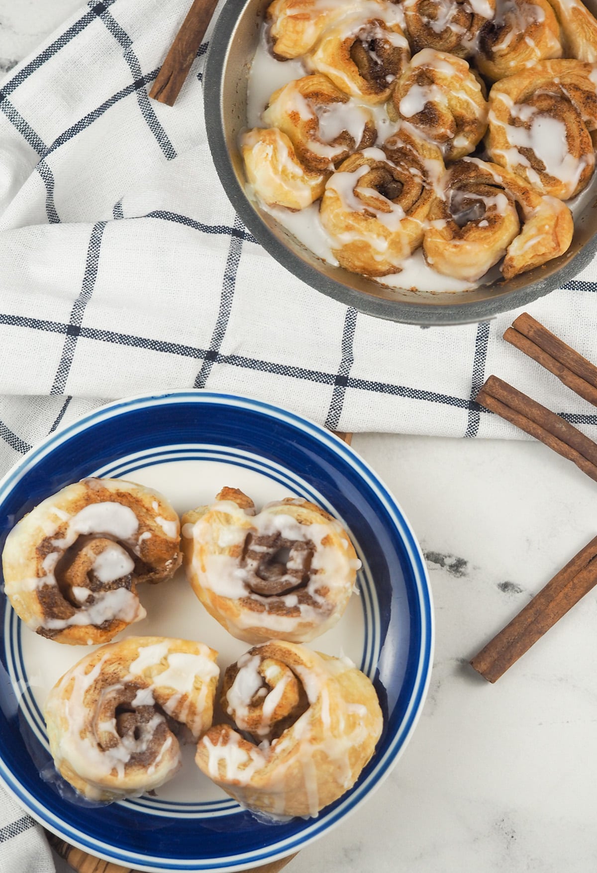 cinnamon rolls on counter with towel on plate and in pie tin with cinnamon sticks