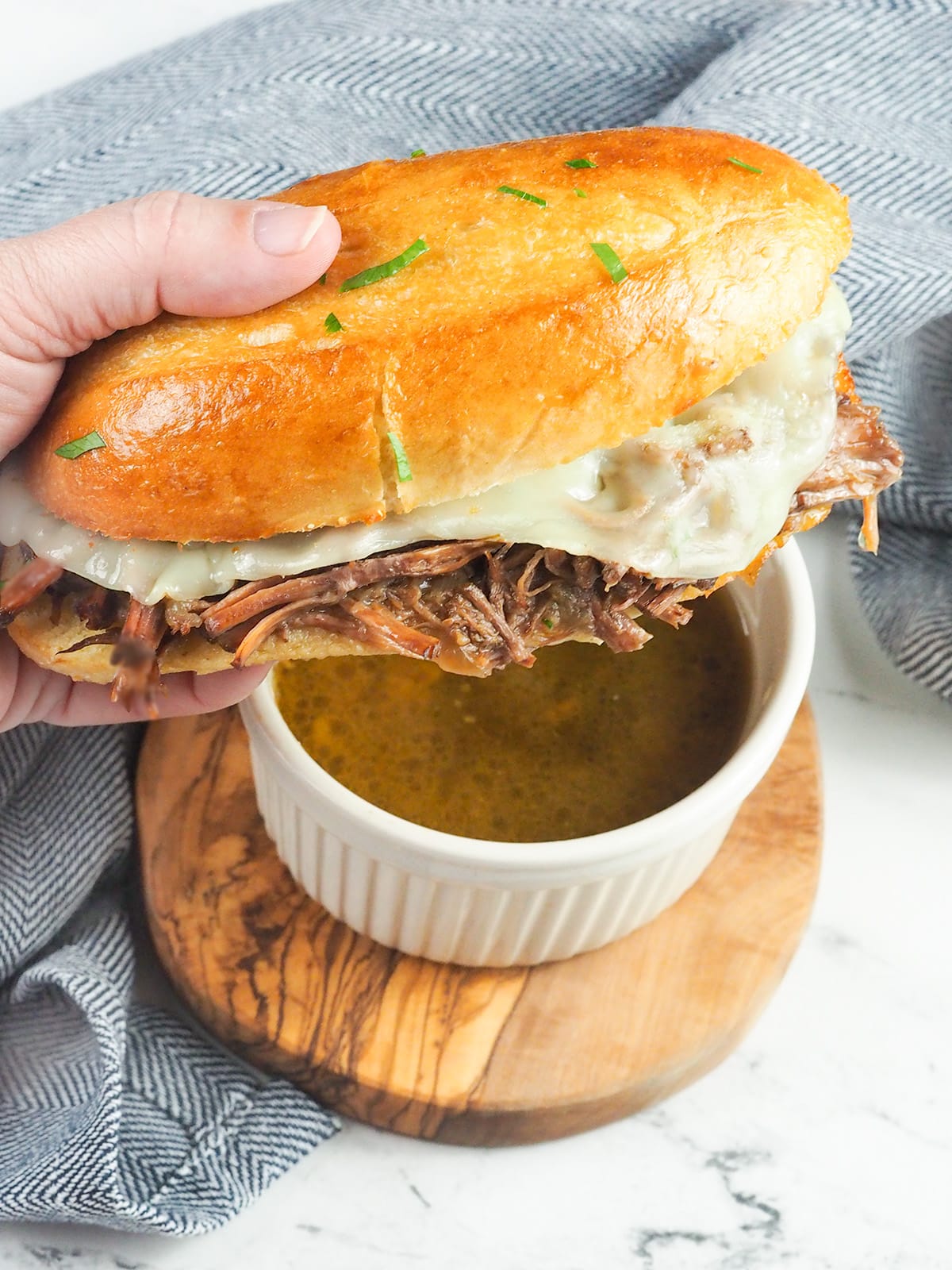 French dip sandwich being held over a ramekin of au jus gravy