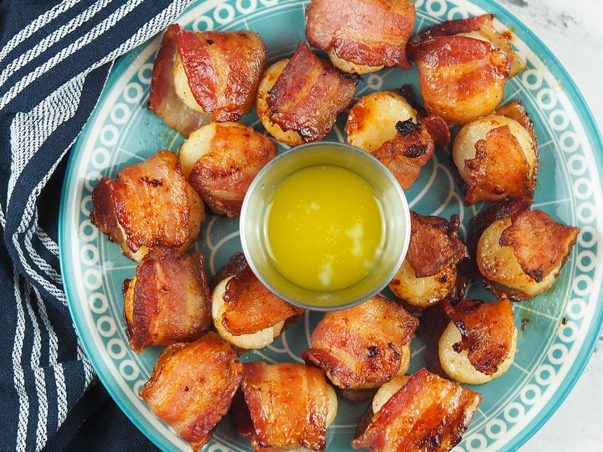 bacon wrapped scallops on blue plate with melted butter