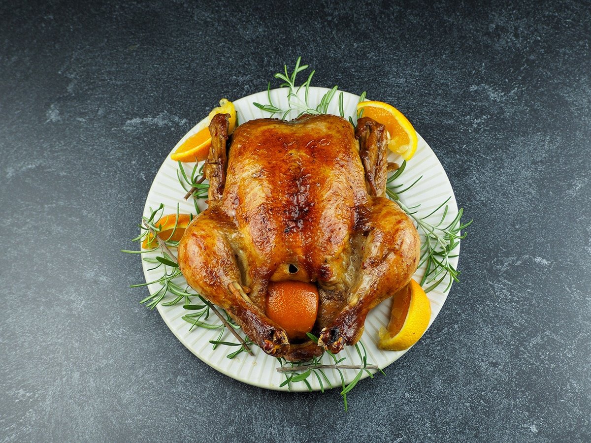 WHOLE CHICKEN ON PLATE WITH ROSEMARY AND ORANGES