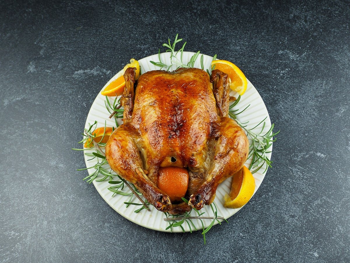 whole chicken on white plate with rosemary and orange wedges