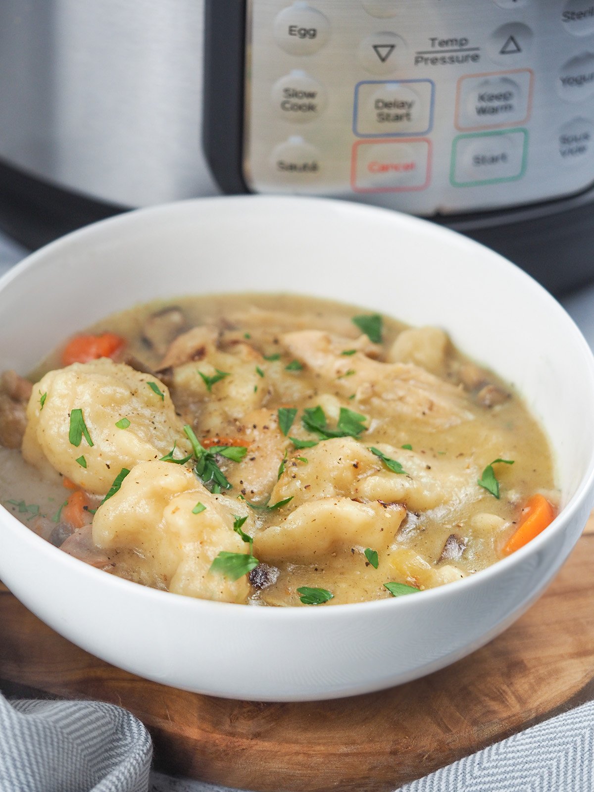 chicken and dumplings in white bowl next to instant pot