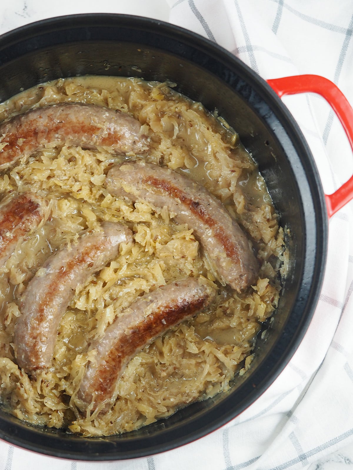 brats nestled in sauerkraut in red handled Dutch oven