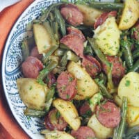 sausage and potatoes with green beans in white bowl with blue designs