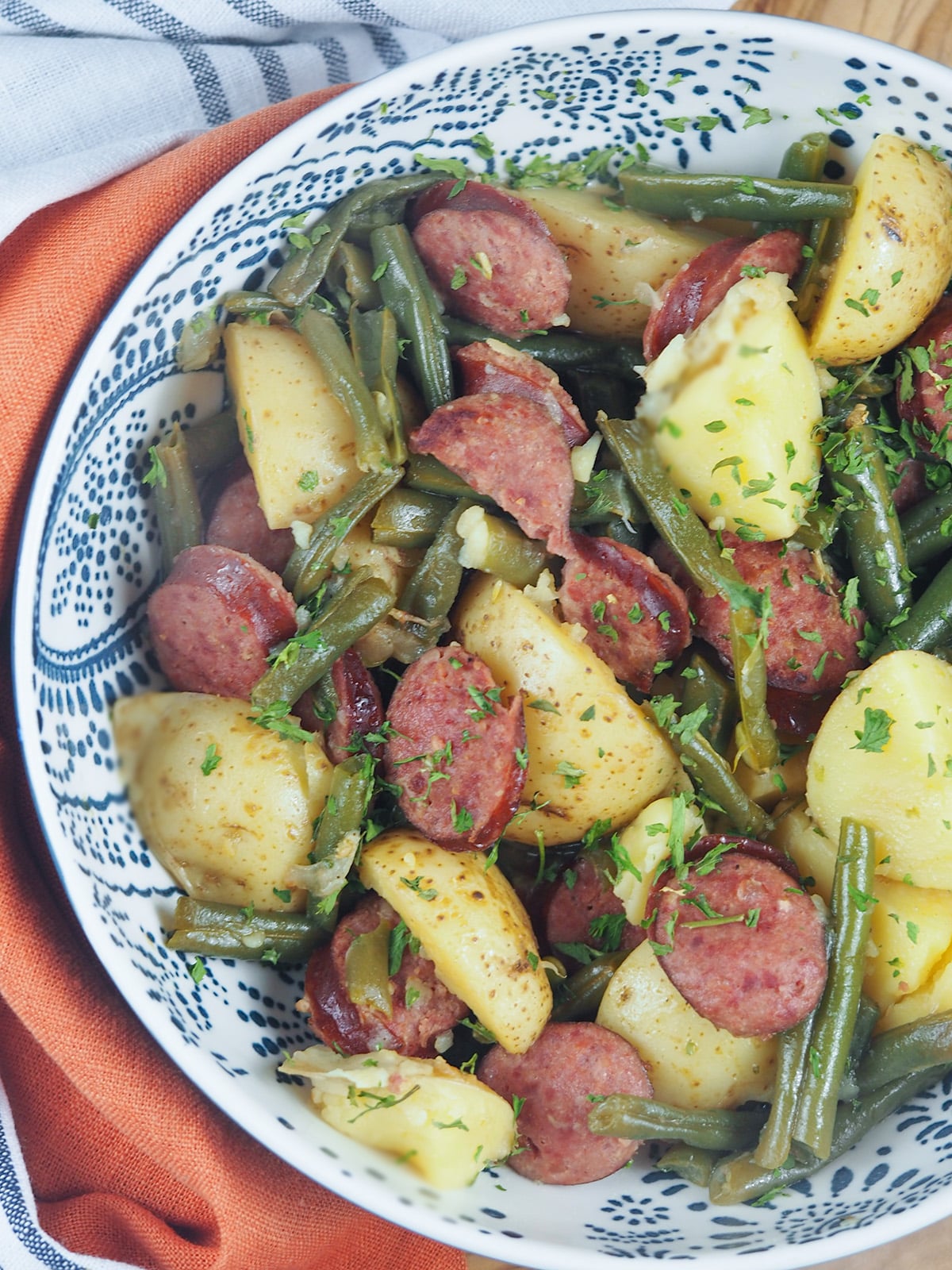 sausage potatoes and green beans in white and blue bowl next to linen towels