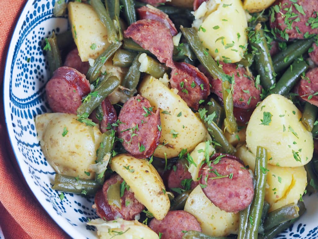 smoked sausage and green beans with potatoes in white bowl with blue designs