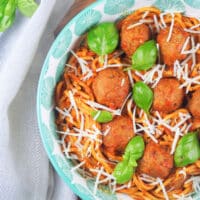 spaghetti with meatballs in bowl sprinkled with parmesan cheese and fresh basil