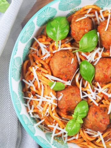 spaghetti with meatballs in bowl sprinkled with parmesan cheese and fresh basil